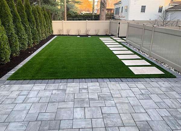 Manicured artificial turf adjacent to elegant paver stones in a private backyard, offering a low-maintenance and evergreen landscaping solution